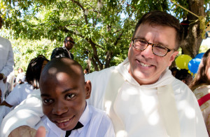 Boy waits with priest during baptism for children abandon during 2010 earthquake in Haiti